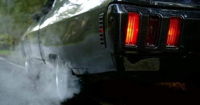 Close-up of the back of a classic car, smoke coming from under the rear wheel.