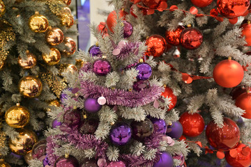 Fototapeta premium Christmas decoration. Golden, purple and red Christmas balls hanging on fir branches. Colorful Christmas ornaments and tinsel garlands on artificial Christmas trees. Luxury holiday decorations. 