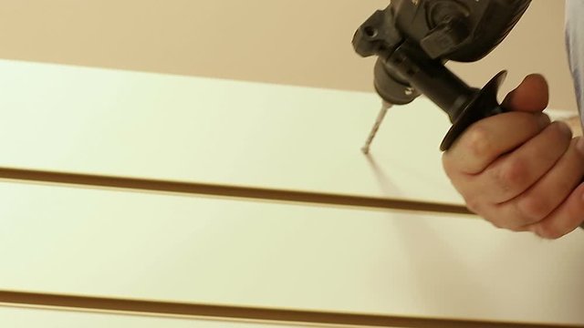 worker makes a hole in the wall covered wooden panel with perforator