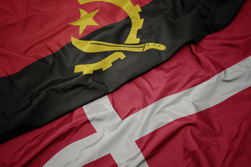 waving colorful flag of denmark and national flag of angola.