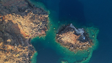 Aerial drone photo of picturesque volcanic with black rock islet and chapel of Agios Nikolaos in bay of Amoudi below iconic village of Oia, Santorini island, Cyclades, Greece