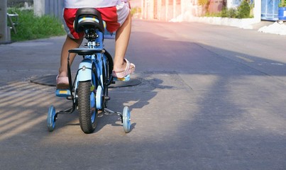 Rear view and low section of child riding bicycle with training wheels on the street in morning time 