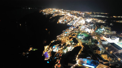 Aerial drone night shot of beautiful illuminated traditional and picturesque village of Oia built on a cliff, Santorini island, Cyclades, Greece