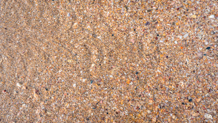 Beach sand texture. Broken seashells background. Colorful sand surface of a beach with clear sea water. Waves.