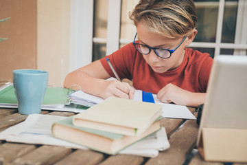 Young student doing homework at home sitting at table outdoor. Boy writing and studying with school...