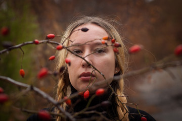autumn portrait of pensive young woman behind the branches of a rosehip bush