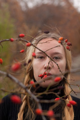 autumn portrait of pensive young woman behind the branches of a rosehip bush