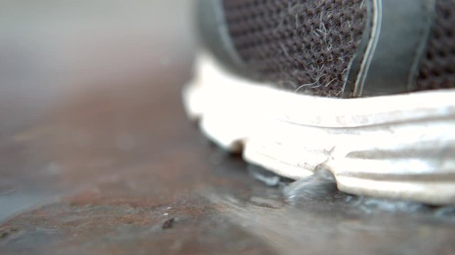 Sole of shoe close up stepping into water puddle slow motion