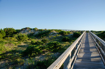 Fototapeta na wymiar Wooden boardwalk crossing the sand dunes heading to the ocean. Oak Island NC beach in the background.