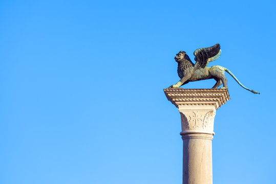 Lion statue at Piazza San Marco (St Mark`s Square) on blue sky background, Venice, Italy. This place is a tourist attraction of Venice city. Winged lion is an ancient and famous symbol of Venice. 