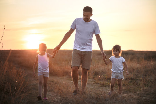 Dad and his daughters in the field at sunset .