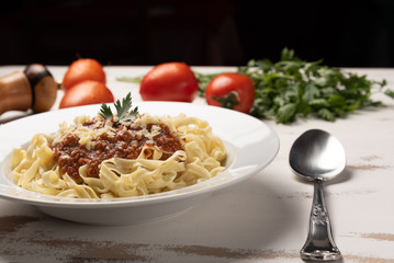 Pasta Fettuccine Bolognese with tomato sauce in a white plate on rustic wooden table background, soft light