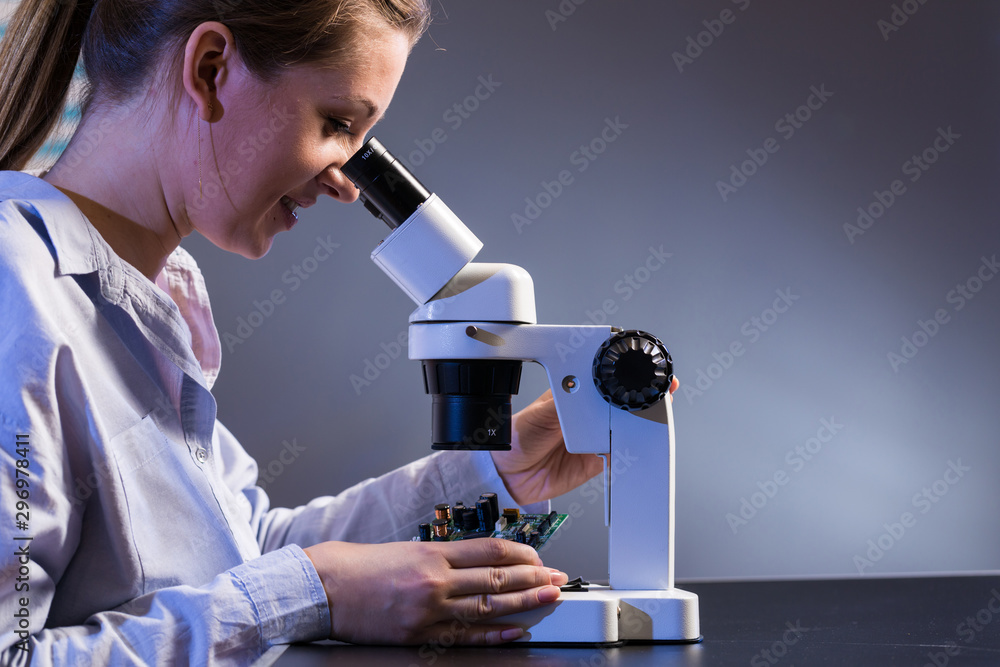 Poster  young woman computer technician testing a printed circuit board with a microscope