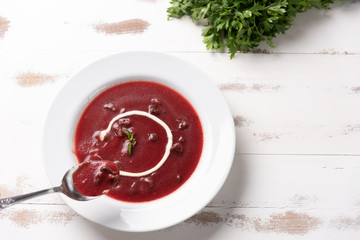 Delicious beet soup with sour cream in a white plate on white wooden table background. Soft light. Traditional Ukrainian Russian borscht beetroot soup