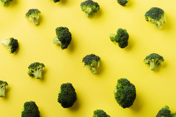 Female hand holds one fresh green broccoli lying on yellow light background. Top view.