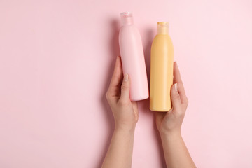 Woman holding blank bottles of cosmetic products on pink background, top view. Space for design