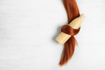Shampoo bottle wrapped in lock of hair on white wooden background, flat lay with space for text....