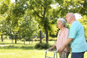 Elderly man helping his wife with walking frame outdoors