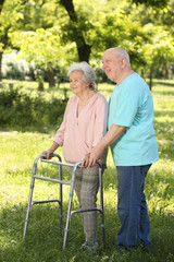 Elderly man helping his wife with walking frame outdoors