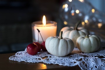 autumn and winter cozy table decoration with candle, small apples and white baby boo pumpkins