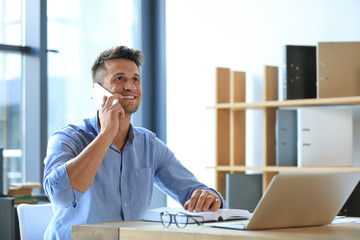 Male business trainer talking on phone while working with laptop in office