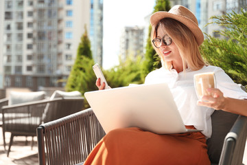 Beautiful woman with laptop and coffee using phone at outdoor cafe