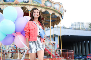 Attractive young woman with color balloons near carousel