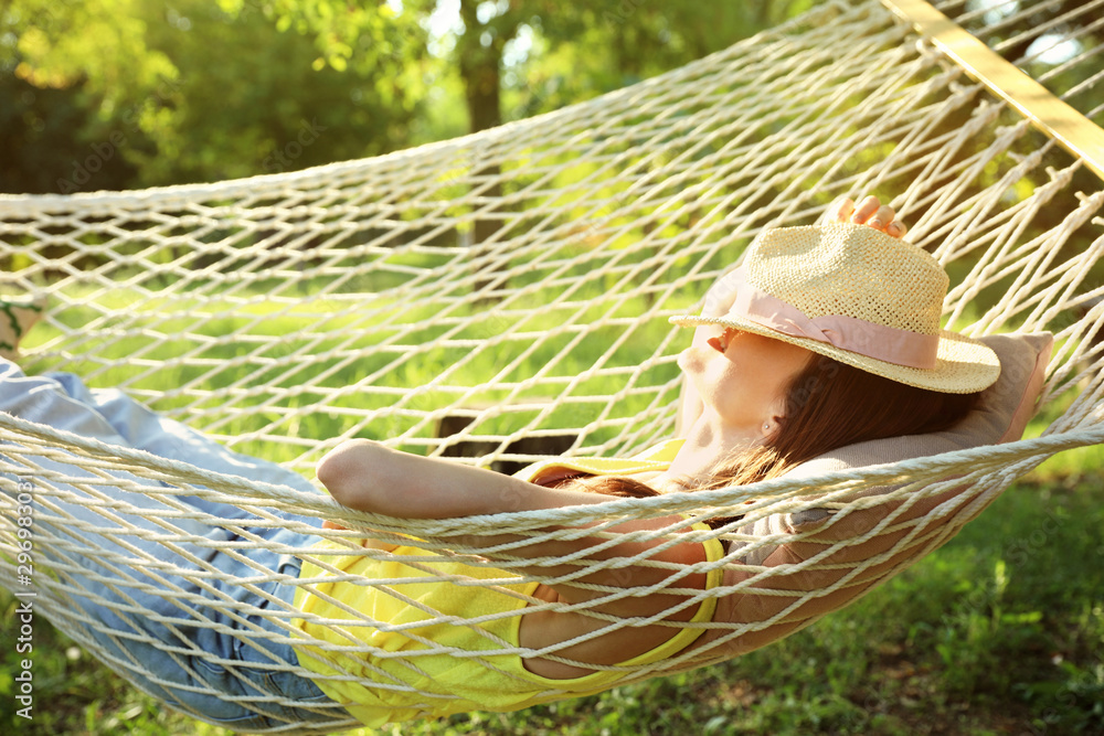 Wall mural Young woman with hat resting in comfortable hammock at green garden