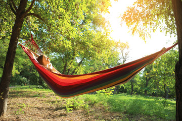 Young woman resting in comfortable hammock at green garden