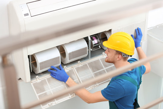 Professional technician maintaining modern air conditioner indoors