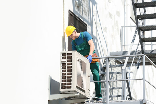 Professional technician repairing modern air conditioner outdoors