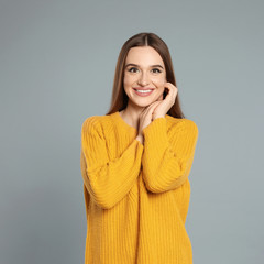 Beautiful young woman in yellow sweater on grey background. Winter season