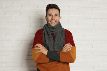 Obraz premium Happy young man in scarf and warm sweater near white brick wall. Winter season