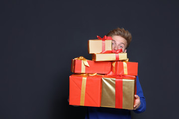Young man with Christmas gifts on dark background. Space for text