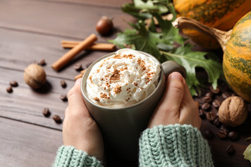 Woman with cup of tasty pumpkin spice latte at wooden table, closeup