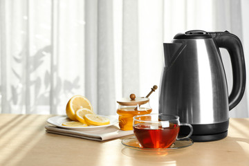 Modern electric kettle and cup of tea on wooden table indoors. Space for text
