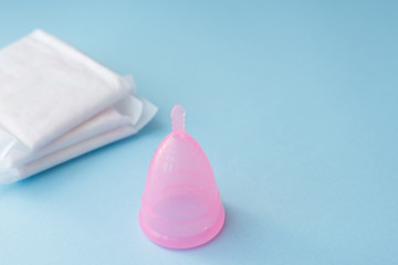 Period products menstrual cup and pads on blue background, copy space