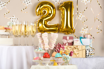 Dessert table in room decorated with golden balloons for 21 year birthday party
