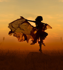 Beautiful dancer woman with flying dress and veil at sunst, orange background.
