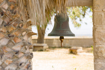 Ritual sacral bell outdoor in garden of a church, next to a palm tree.