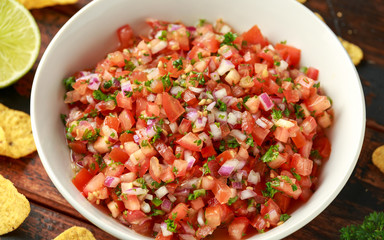 Mexican Tomato Salsa in white bowl with lime, red onion, jalapeno pepper, parsley and tortilla chips on wooden table