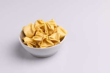 Fagottini Tortellini pasta in a white bowl isolated in white background, soft light, studio photo