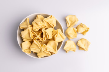 Fagottini Tortellini pasta in a white bowl isolated in white background, soft light, studio photo