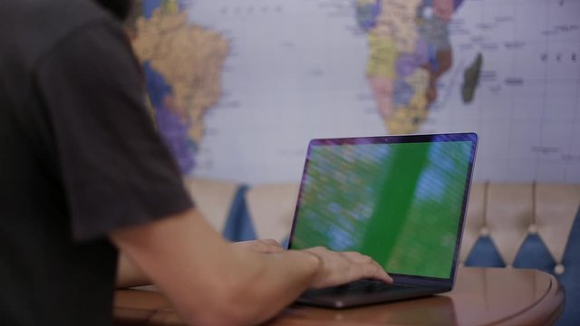 Close-up of male hands typing at laptop, background of world map.