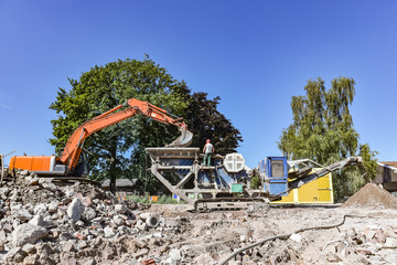 Bagger füllt Steine in eine Steinmühle auf einer Abrissbaustelle