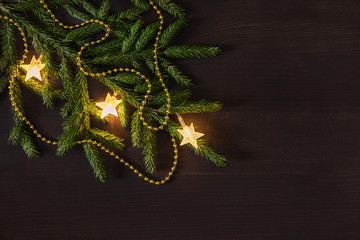 Christmas still life of garland, spruce branches and gold beads. Christmas background on dark wooden table. Flat lay, top view, copy space. Christmas concept