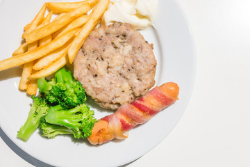 Minced Pork Steak, Sausage and bacon roll with French Fries and broccoli on the plate isolated close up on white background from top-view