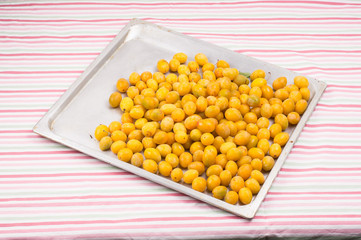 yellow fresh ripe plums placedon on aluminum tray on table with colorful striped tablecloth. Vegetarian or healthy eating.