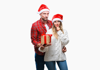 Young couple in love wearing christmas hat and holding present over isolated background serious face thinking about question, very confused idea