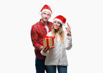 Young couple in love wearing christmas hat and holding present over isolated background surprised with an idea or question pointing finger with happy face, number one